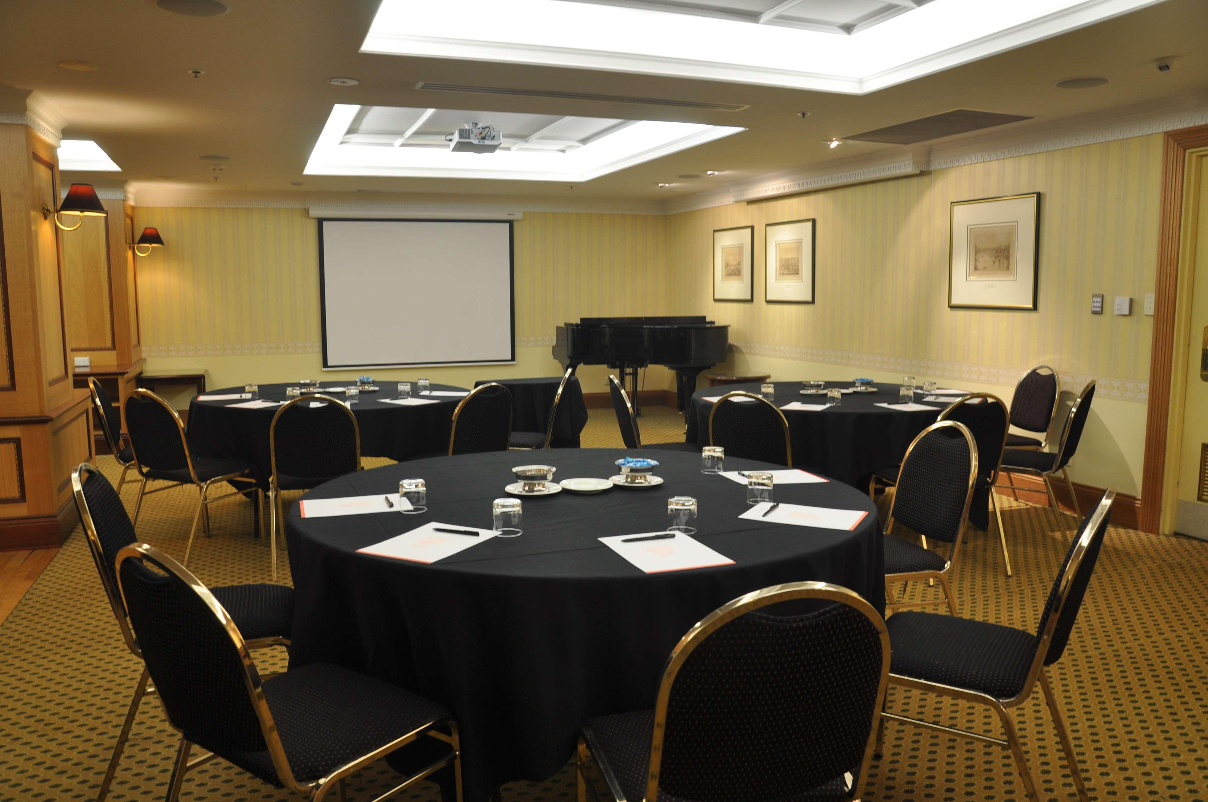 Stamford Plaza Adelaide Hotel Luaran gambar The photo shows a conference room set up for a meeting or presentation. There are several round tables covered with black tablecloths, each surrounded by black upholstered chairs. On the tables, there are notepads and glasses of water, indicating tha