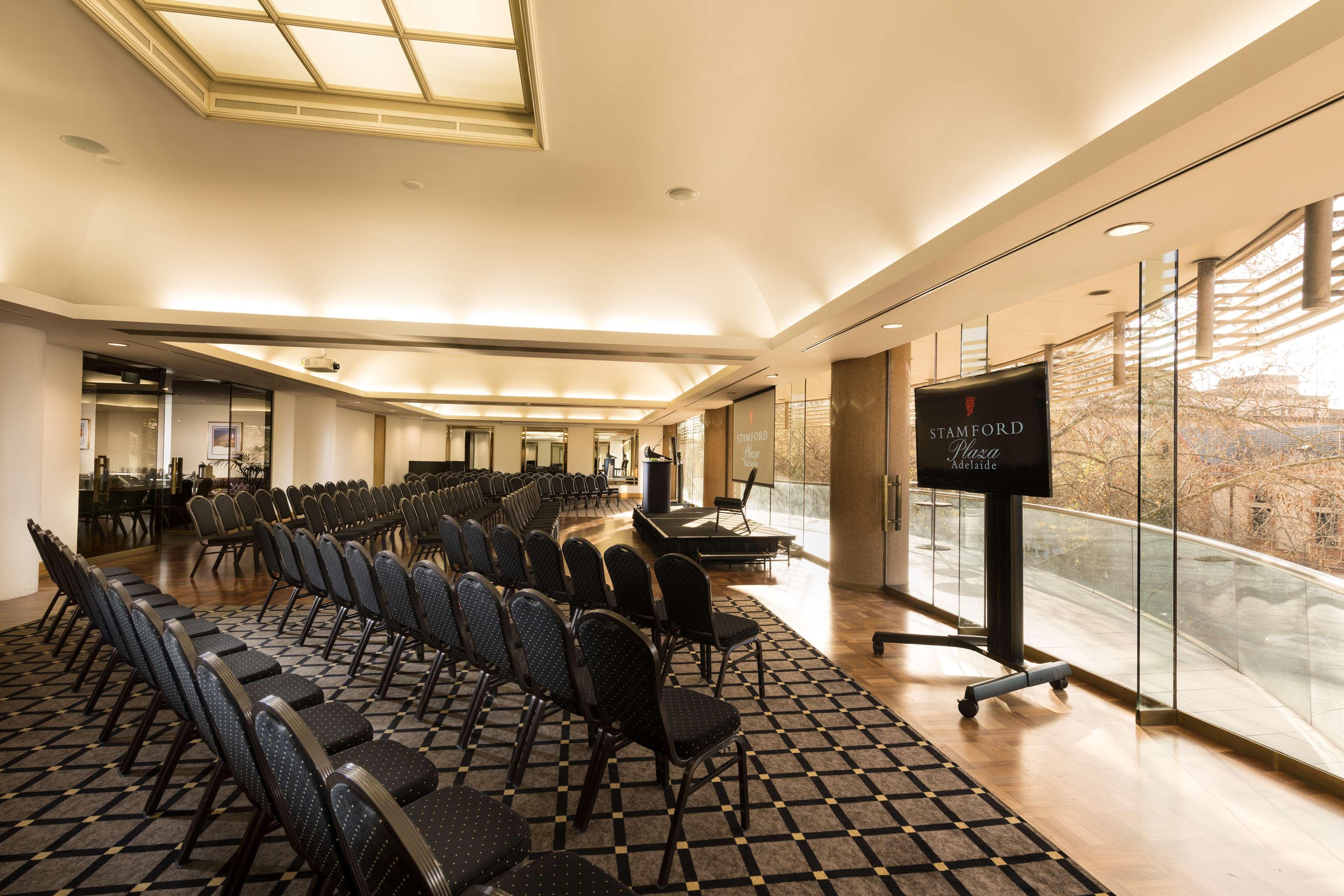 Stamford Plaza Adelaide Hotel Luaran gambar The photo shows a large, elegantly designed event space or meeting room. There are rows of black chairs set up facing a presentation area. The flooring features a patterned carpet, and large windows allow natural light to enter the room. On one side,