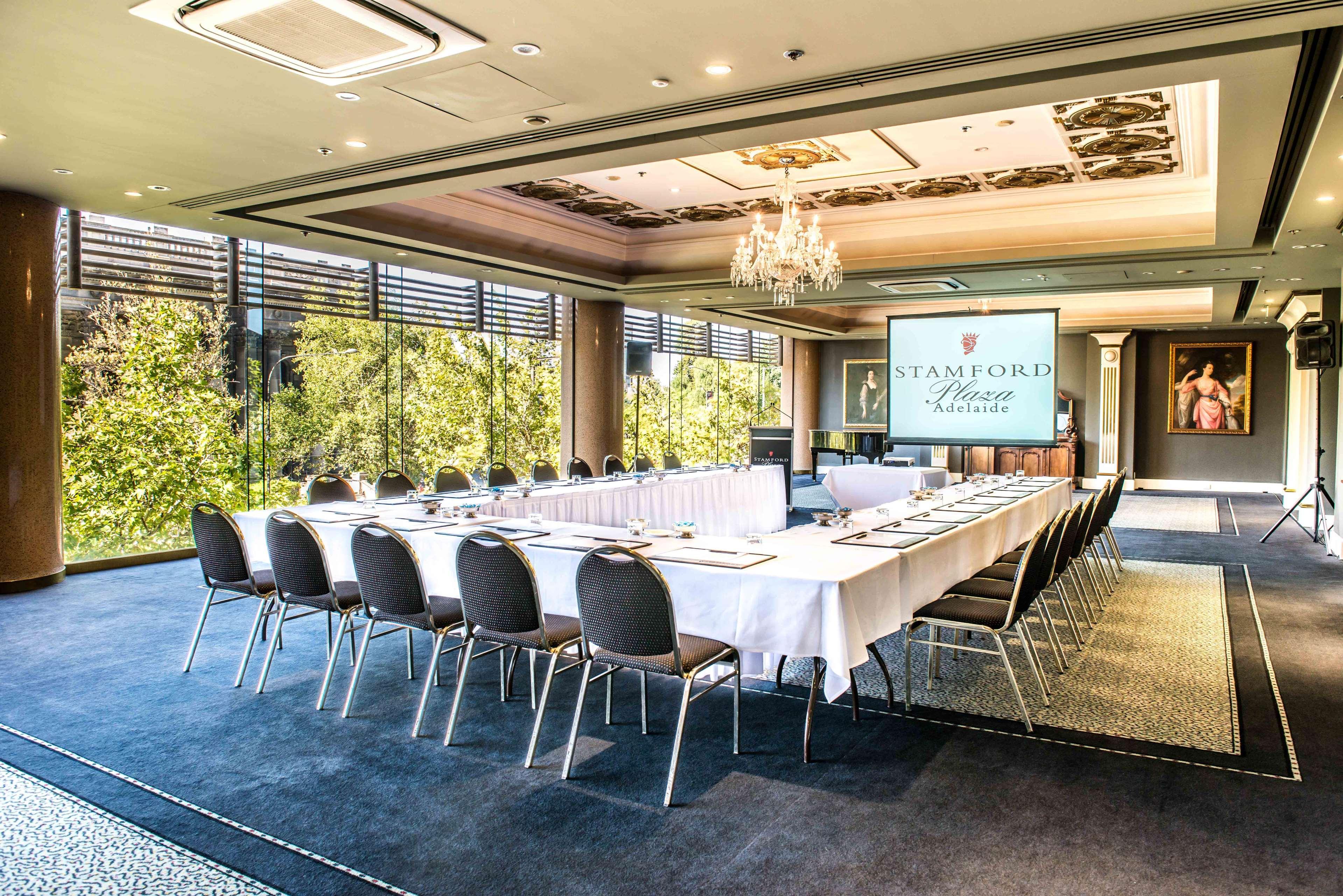 Stamford Plaza Adelaide Hotel Luaran gambar The photo shows a stylish conference room set up for a meeting or event. There is a long rectangular table covered with a white tablecloth, surrounded by black chairs. A large screen displays the name "Stamford" along with a logo. The room features l